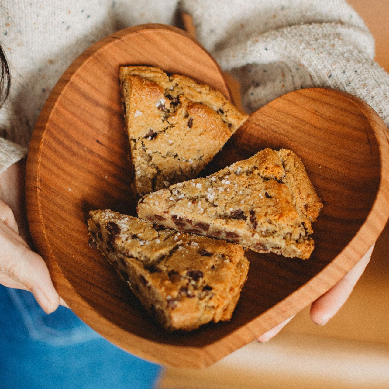 Heart-shaped wooden plate with triangular cookies held by a person wearing a speckled sweater.