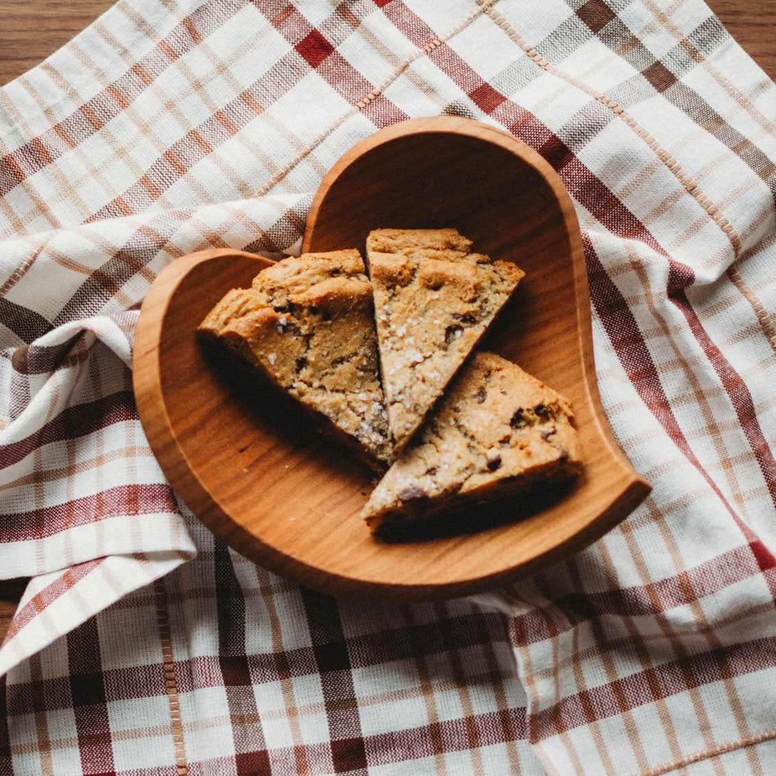 Wooden heart-shaped plate with scones on a plaid cloth