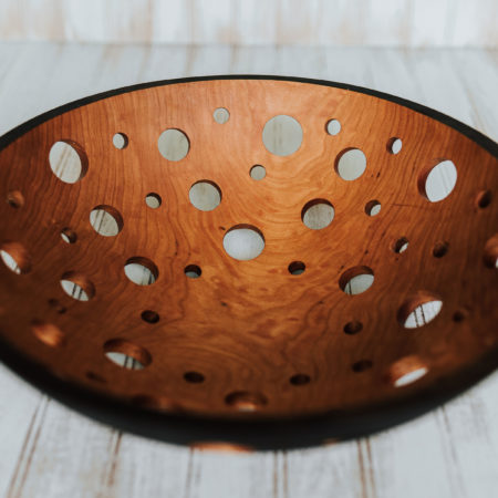 A 15-inch ebonized wooden fruit bowl with holes for aeration