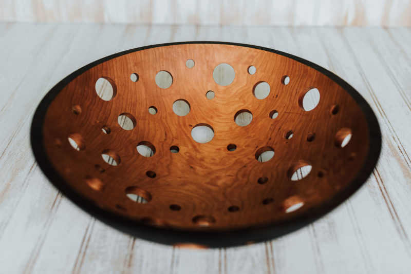 A 15-inch ebonized wooden fruit bowl with holes for aeration