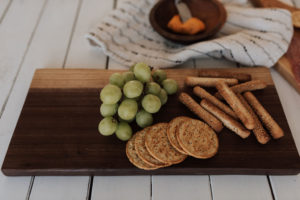 A wood cytting and serving board by the Holland Bowl Mill, with grapes, crackers, pretzels, and spreading cheese. Fixing a warped cutting board takes time, but with proper care, can be easily achieved.