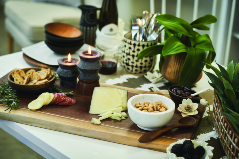 A charcuteries setup with various meats, cheeses, jams and vegetables sit on a double live edge wood cutting board.