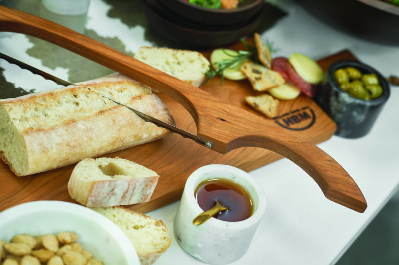 Cherry wood bread board and knife set. A bow knife slices into fresh-baked French bread