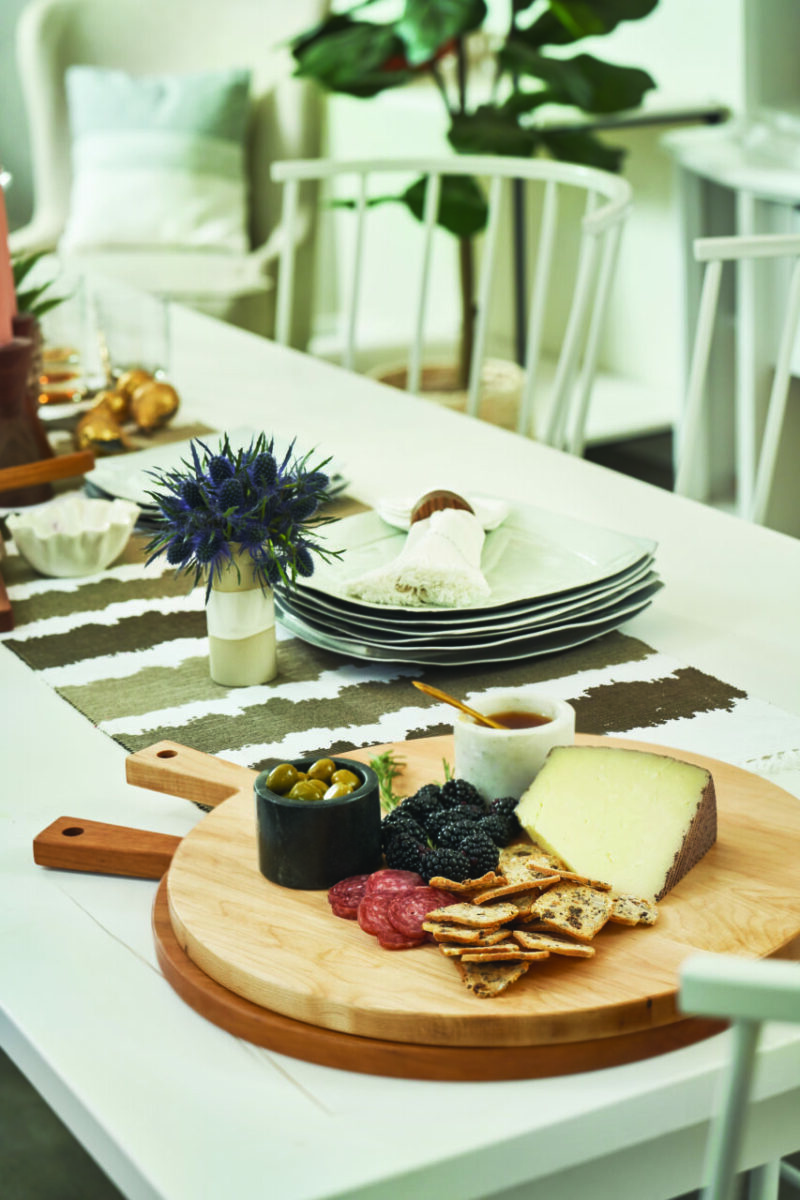 Two round wooden serving boards rest on a dining room table. Assorted berries, cheese, crackers, and meats sit on the boards.