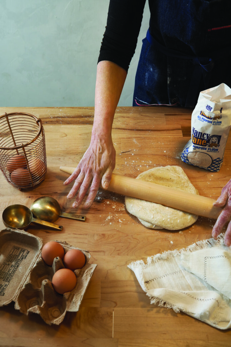 A baker rolls dough on a kitchen counter with her French rolling pin.