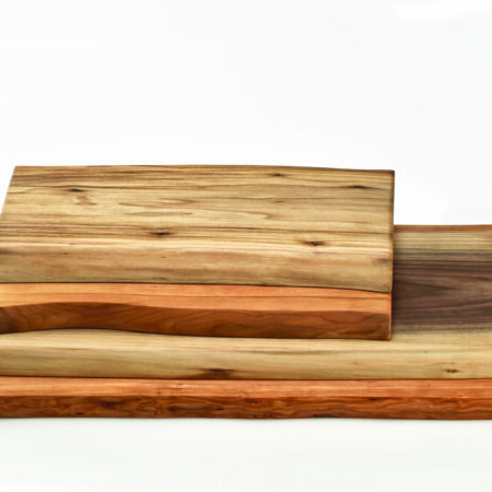 A small double live edge wood cutting board sits atop another. Known for their rustic style