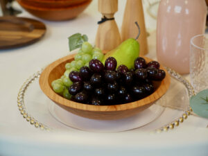Green grapes, purple grapes and a pear sit in a wooden bowl on a table, next to wooden salt and pepper shakers.
