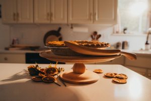 Natural wood cake stand displaying homemade pie in warm kitchen setting with wooden cutting boards and dried citrus decorations